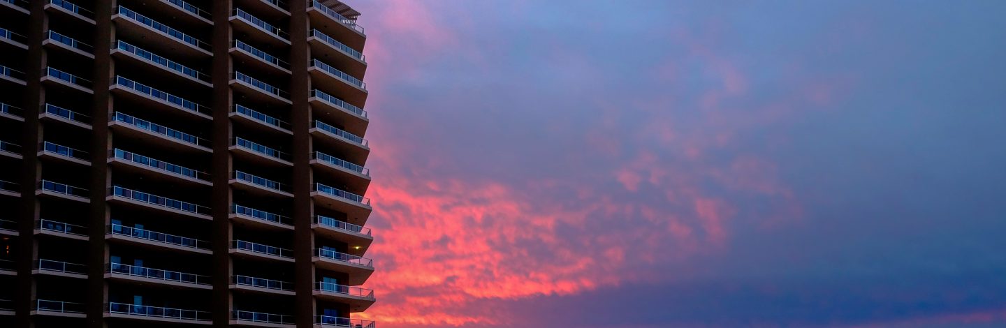 Large building on the left with sun setting and sea on the right