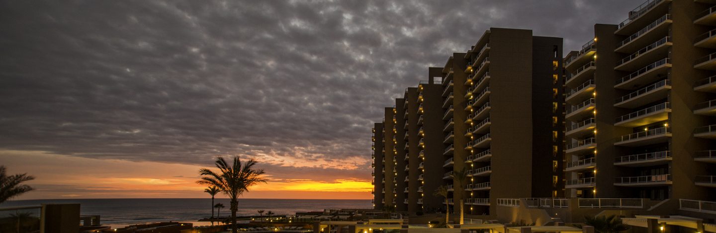 Buildings on the right with the sunset and the sea on the left side.