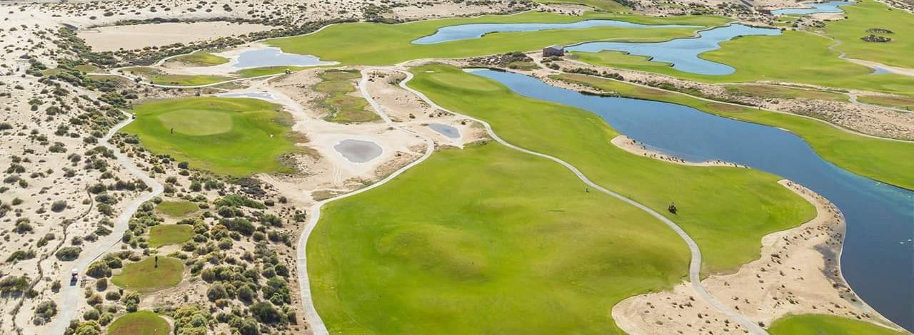 Golf course surrounded by sand with buildings in the distance