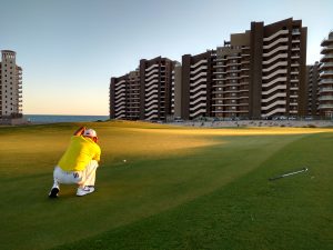 Crouching man in a golf course overlooking buildings
